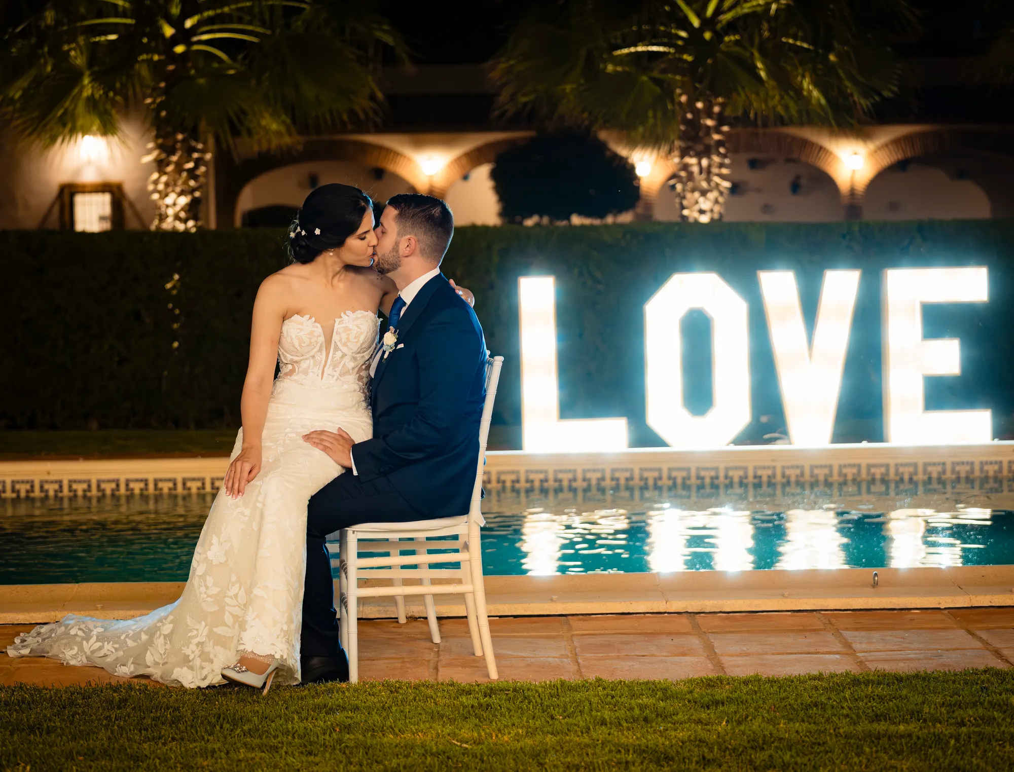 Novios besándose junto a la piscina y unas letras luminosas