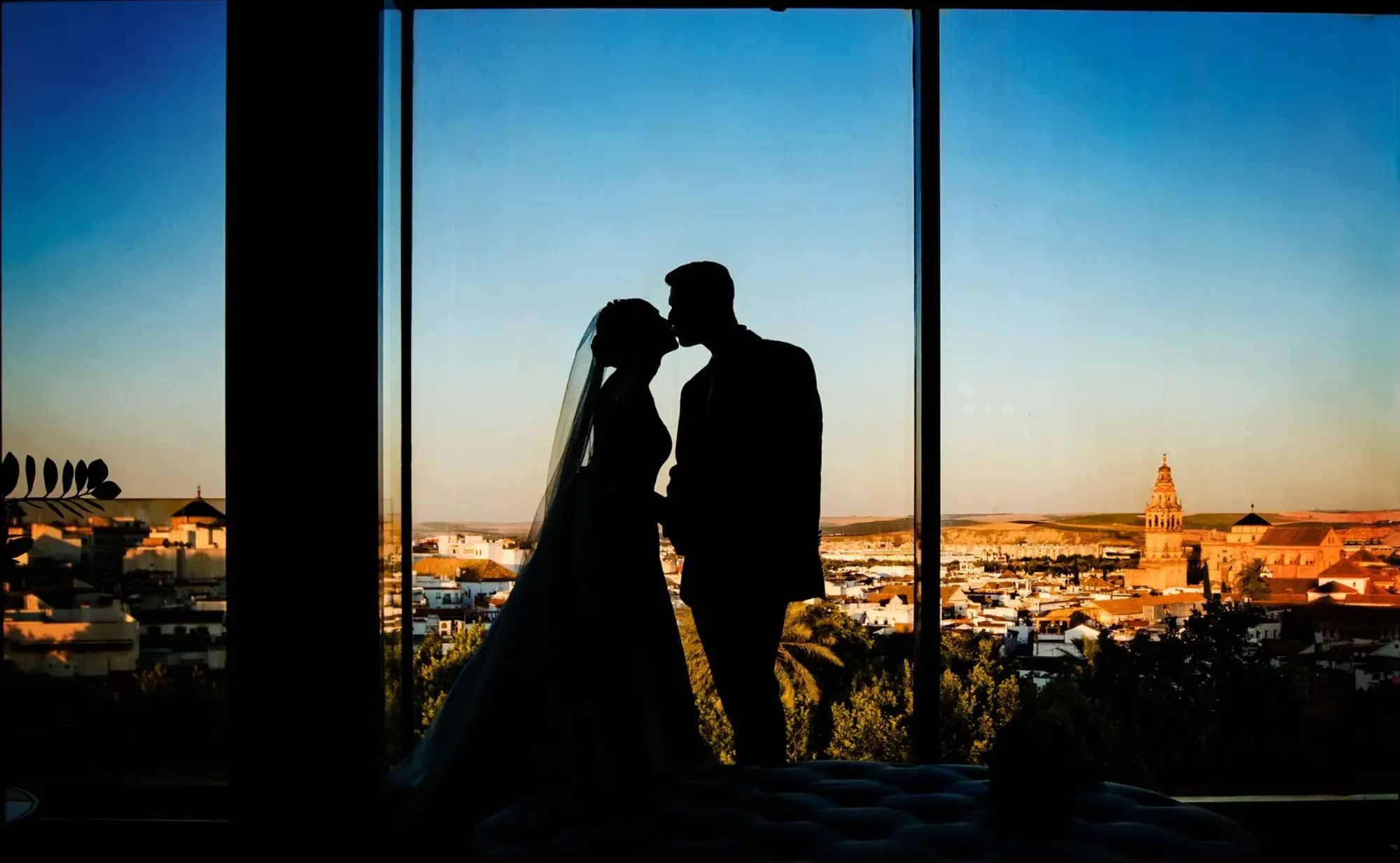 Silueta de los novios besándose ante una ventana con vistas a la ciudad