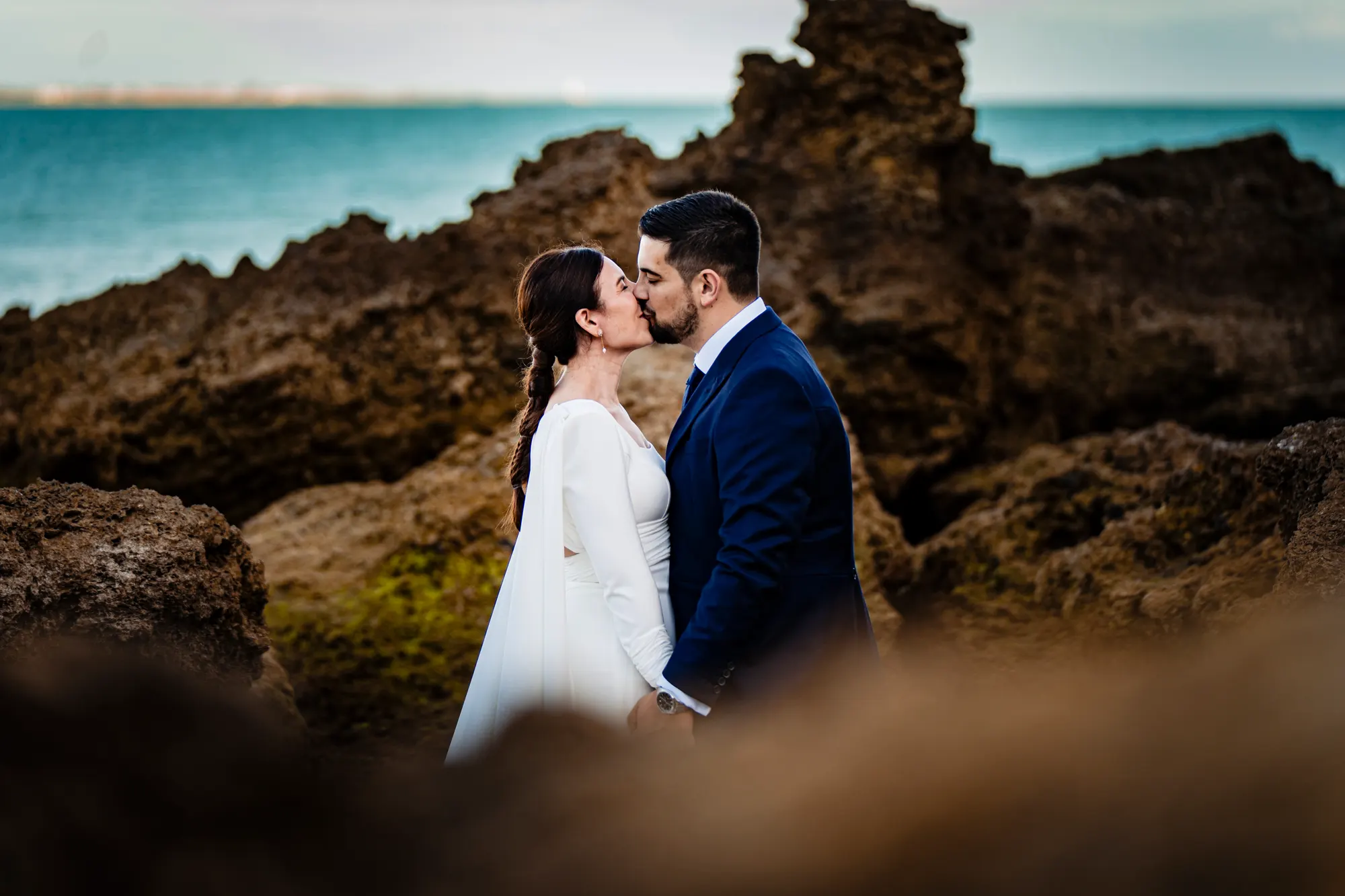 Novios besándose entre rocas junto al mar
