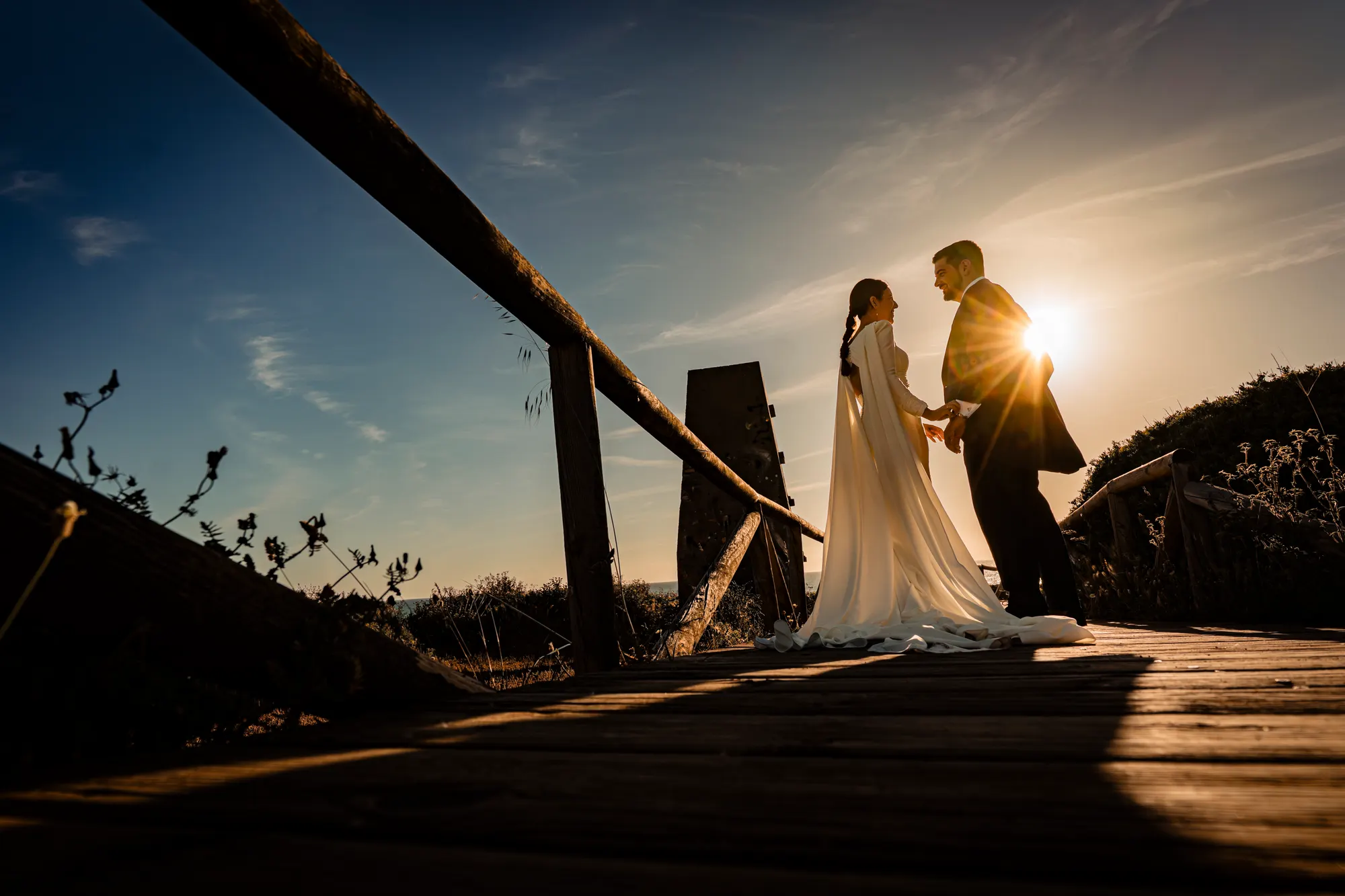 Novios a contraluz sobre una pasarela de madera