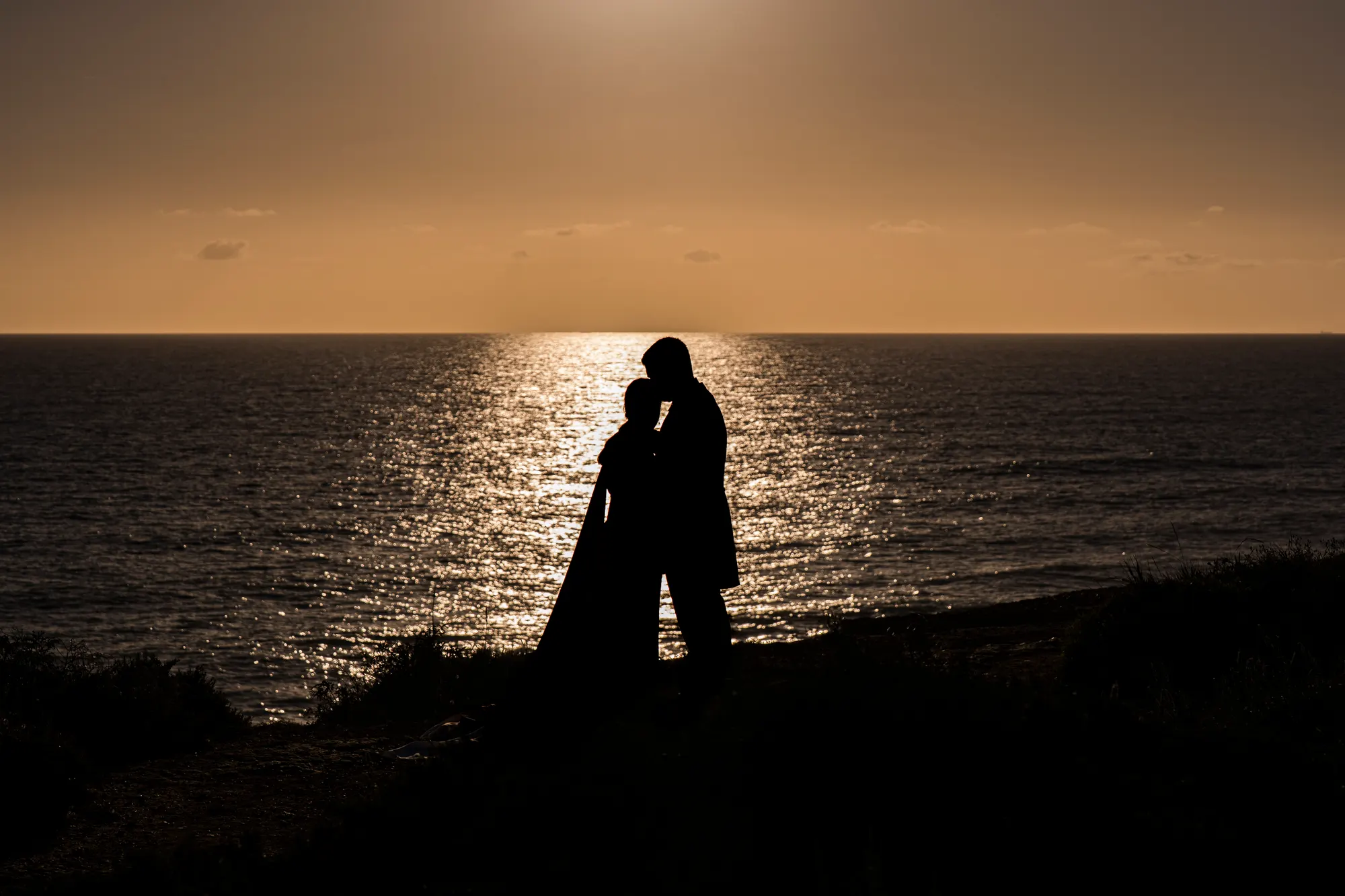 Silueta de los novios besándose frente al mar al atardecer