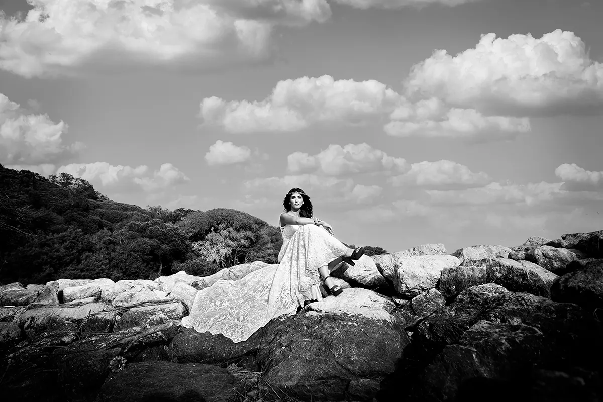 Novia recostada sobre las rocas bajo un cielo de nubes