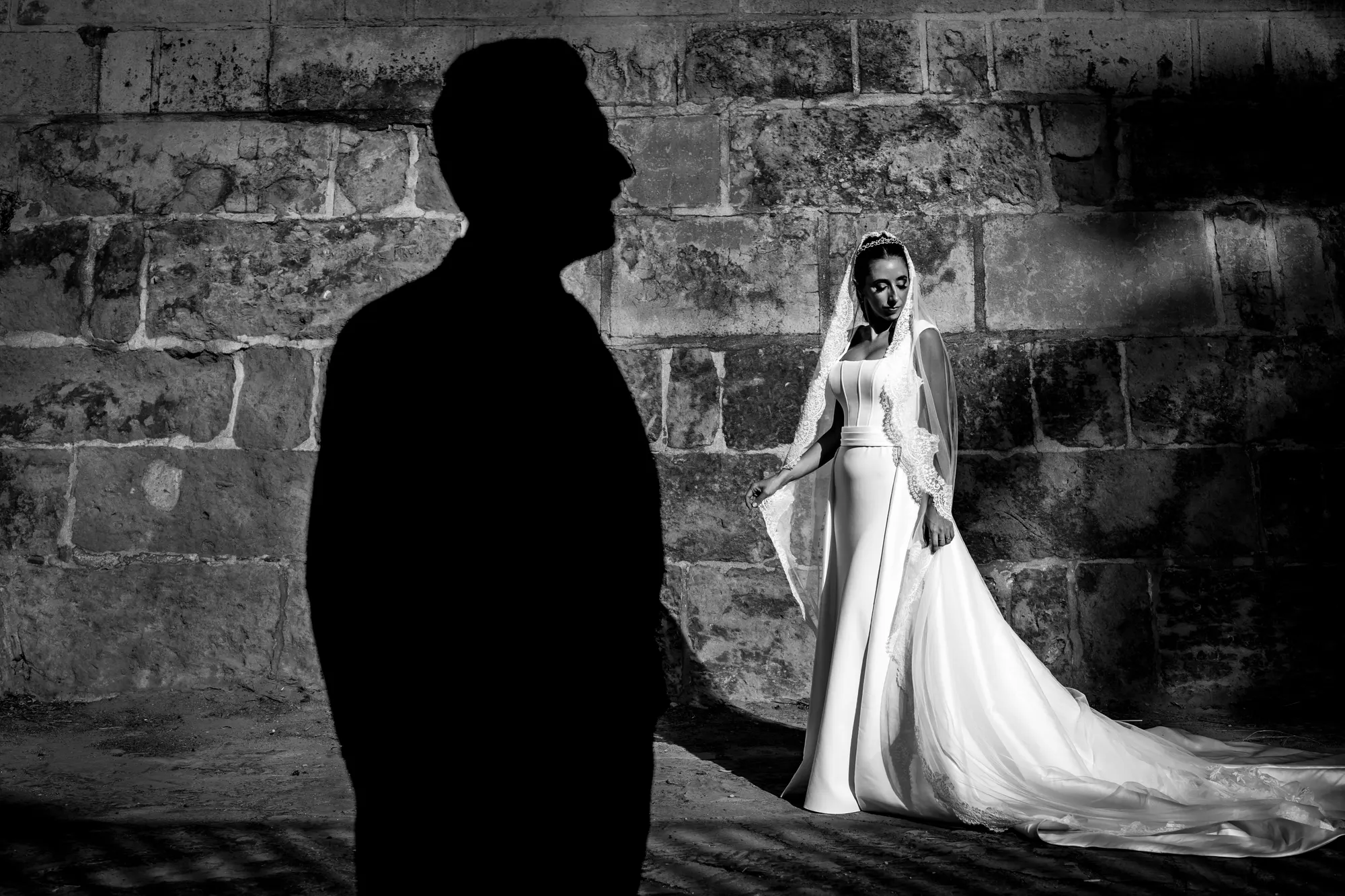 Silueta del novio mirando a la novia ante un muro de piedra