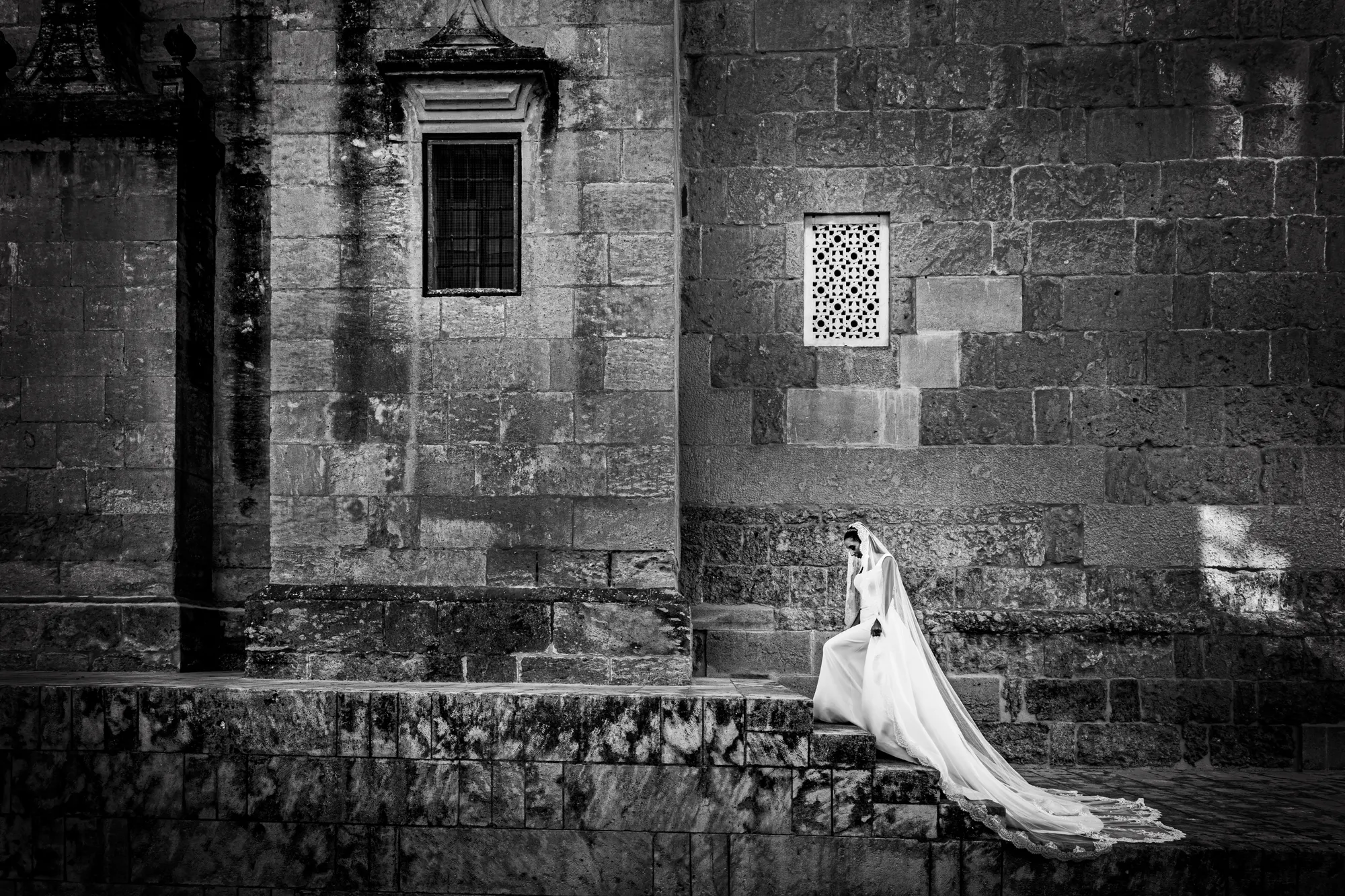 Novia sentada junto a un muro de piedra histórico