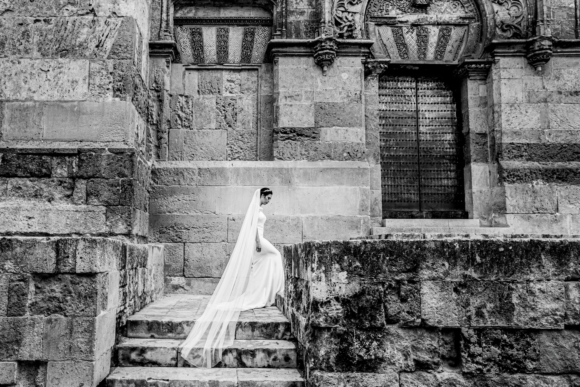 Novia sentada en una escalinata de piedra, en blanco y negro