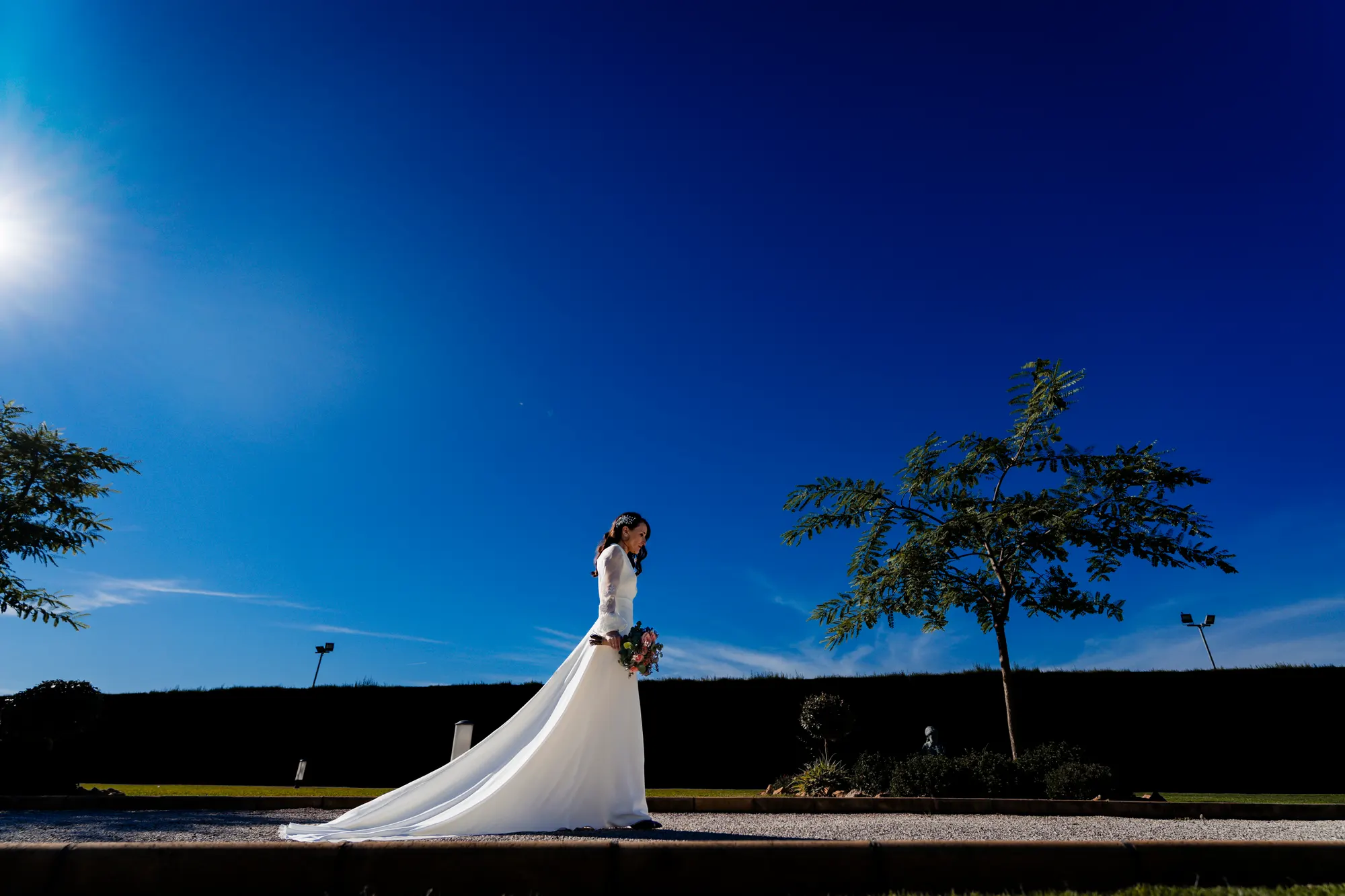 Novia con vestido de cola bajo un cielo azul intenso