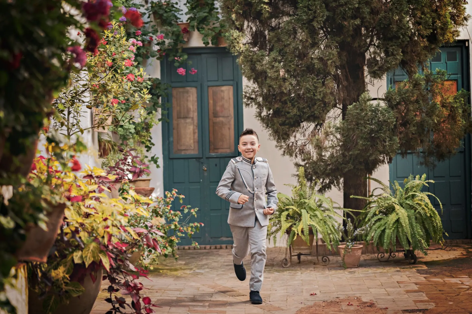 Niño de comunión corriendo en un patio con flores
