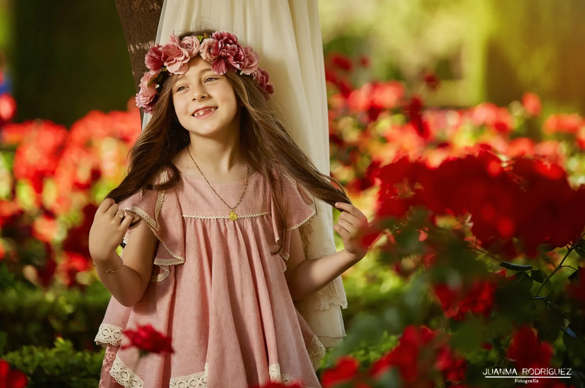 Niña con corona de flores entre rosas rojas