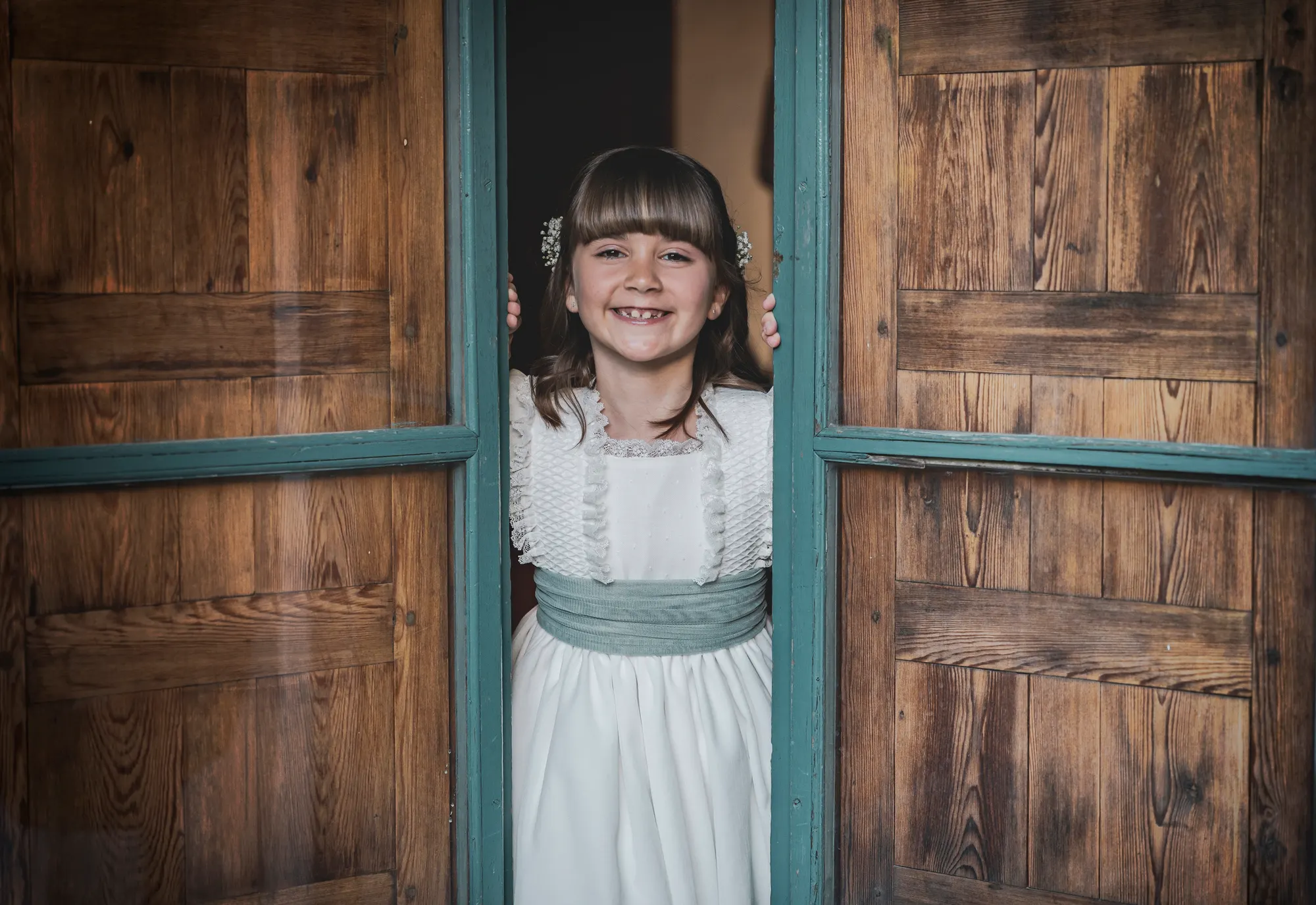 Niña asomada entre dos puertas de madera