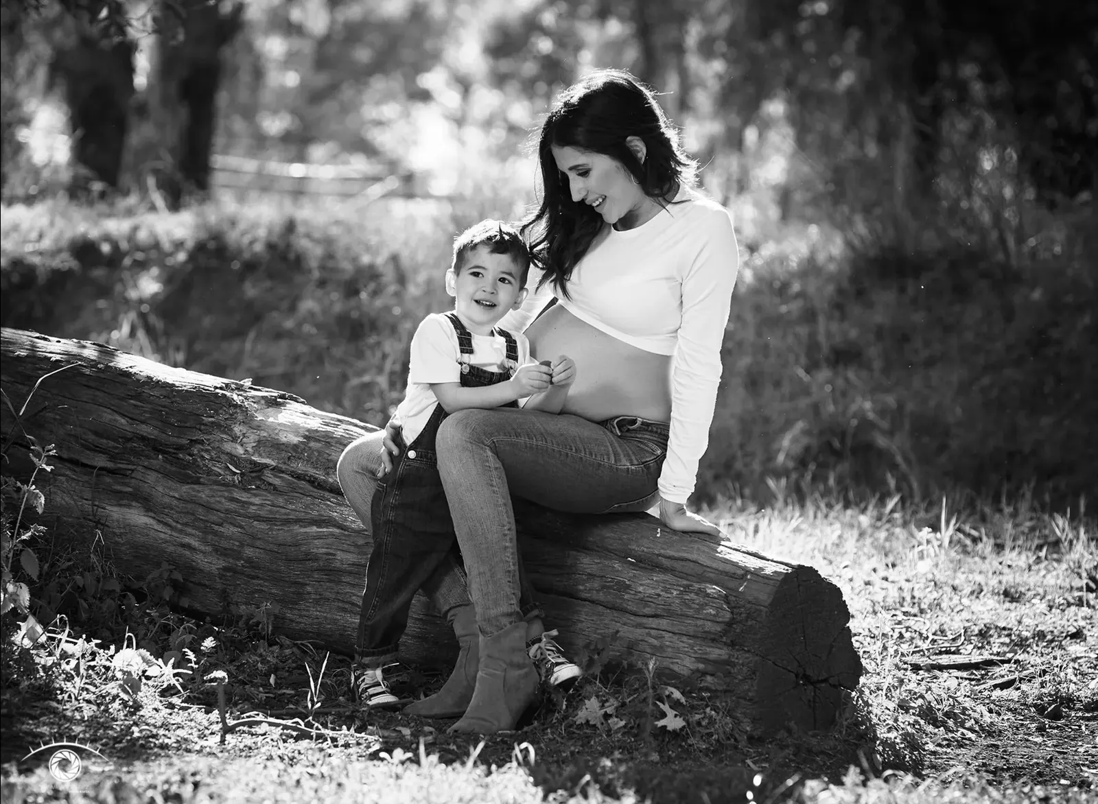 Mamá embarazada con su hijo sobre un tronco, en blanco y negro
