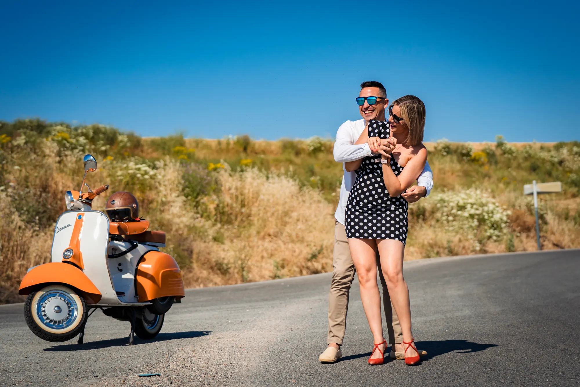 Pareja junto a una Vespa naranja en una carretera de campo
